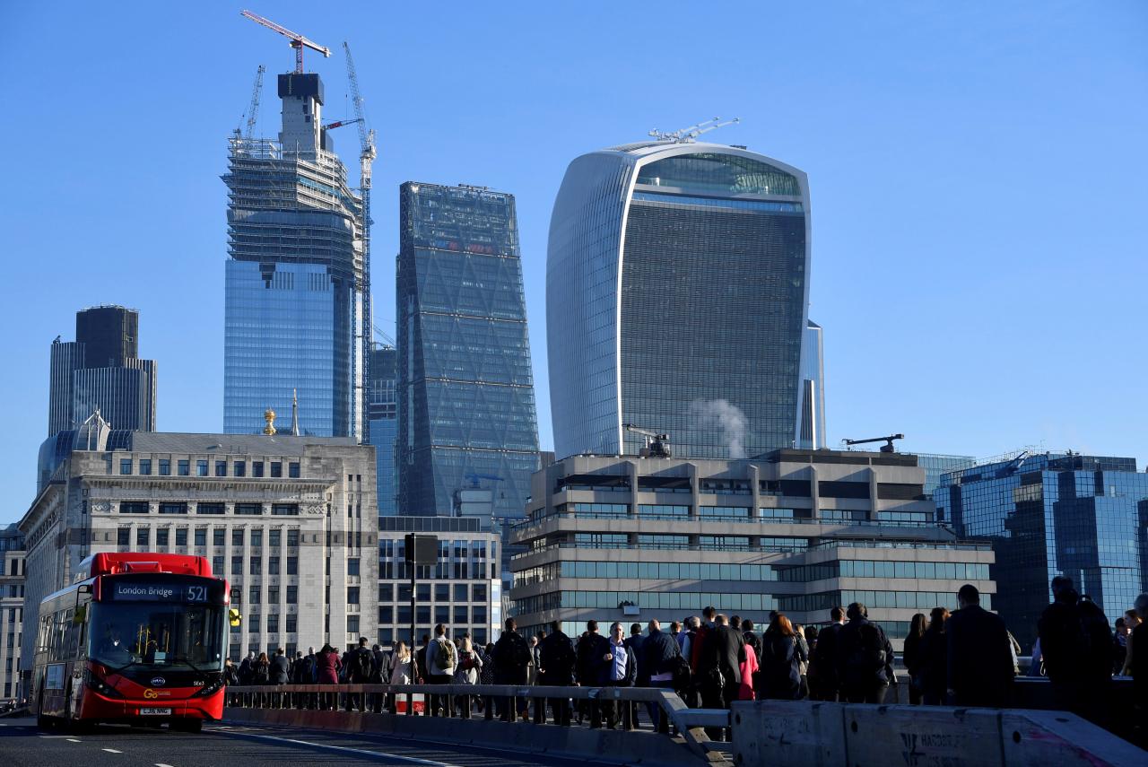 Workers are seen crossing London Bridge with City of London skyscrapers seen behind during the morning rush hour in London