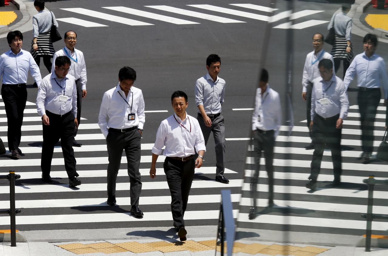 FILE PHOTO: Office workers are reflected in a glass railing as they cross street during lunch hour in Tokyo