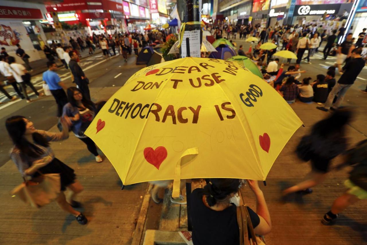 A woman sits under a yellow umbrella as pro-democracy protesters gather on a main street they occupy at Mongkok shopping district in Hong Kong