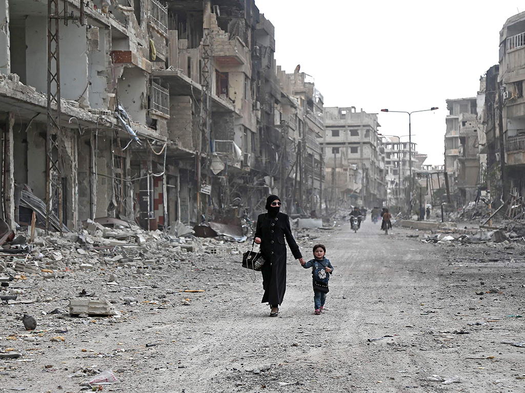 A Syrian woman and child walk down a destroyed street as civilians and rebels prepare to evacuate one of the few remaining rebel-held pockets in Arbin, in Eastern Ghouta, on the outskirts of the Syrian capital Damascus, on March 24, 2018.